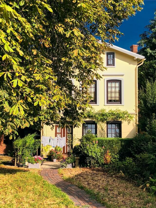 Gelbfarbenes Haus mit Vorgarten und einem Baum im Blickfeld